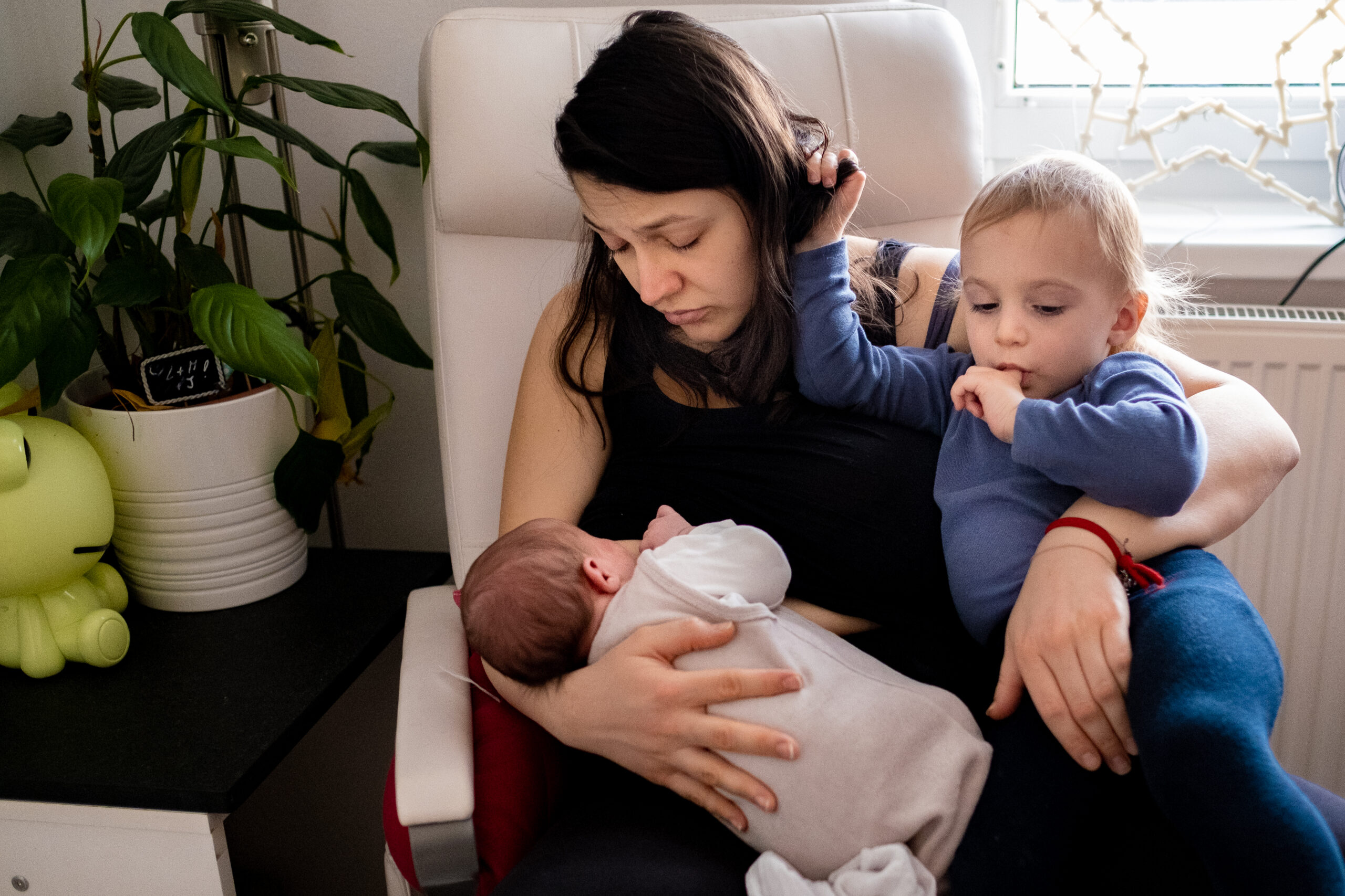 Mutter im Wochenbett mit Kleinkind und Neugeborenem beim Stillen